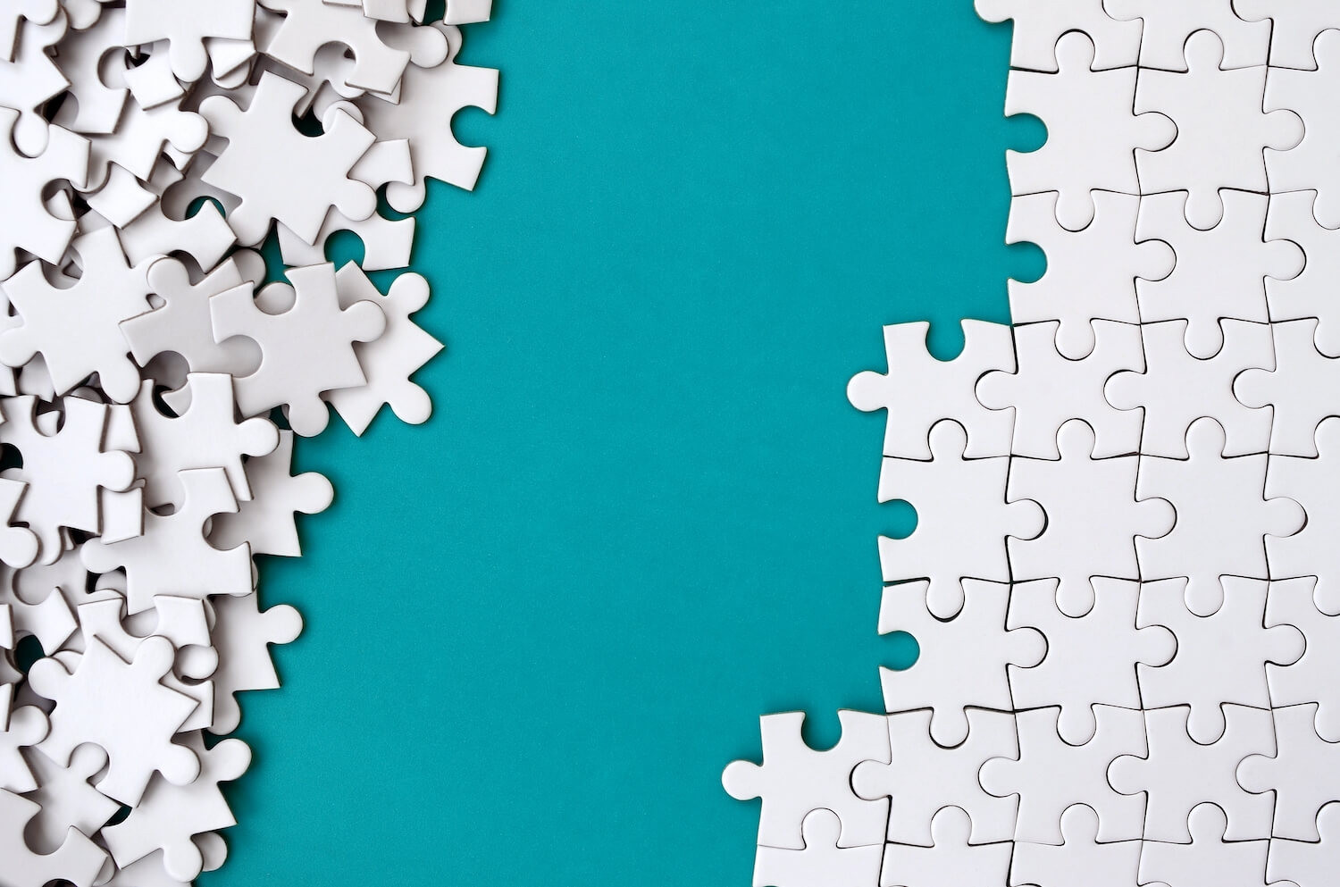 Fragment of a folded white jigsaw puzzle and a pile of uncombed puzzle elements against the background of a blue surface. Texture photo with space for text Fragment of a folded white jigsaw puzzle and a pile of uncombed puzzle elements against the background of a blue surface. Texture photo with space for text