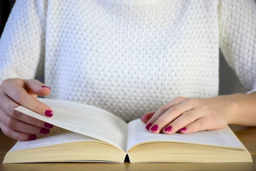 Young woman with manicure sitting at the table and reading book