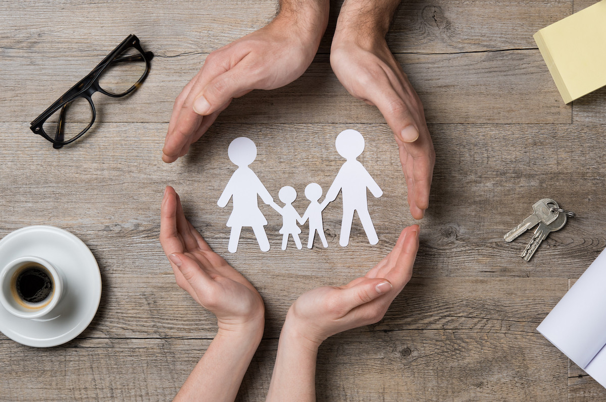 Close up of female and male hands protecting a paper chain family. Top view of two hands form a circle around white paper chain family on wooden table. Family care, insurance and helping hand concept. Family care